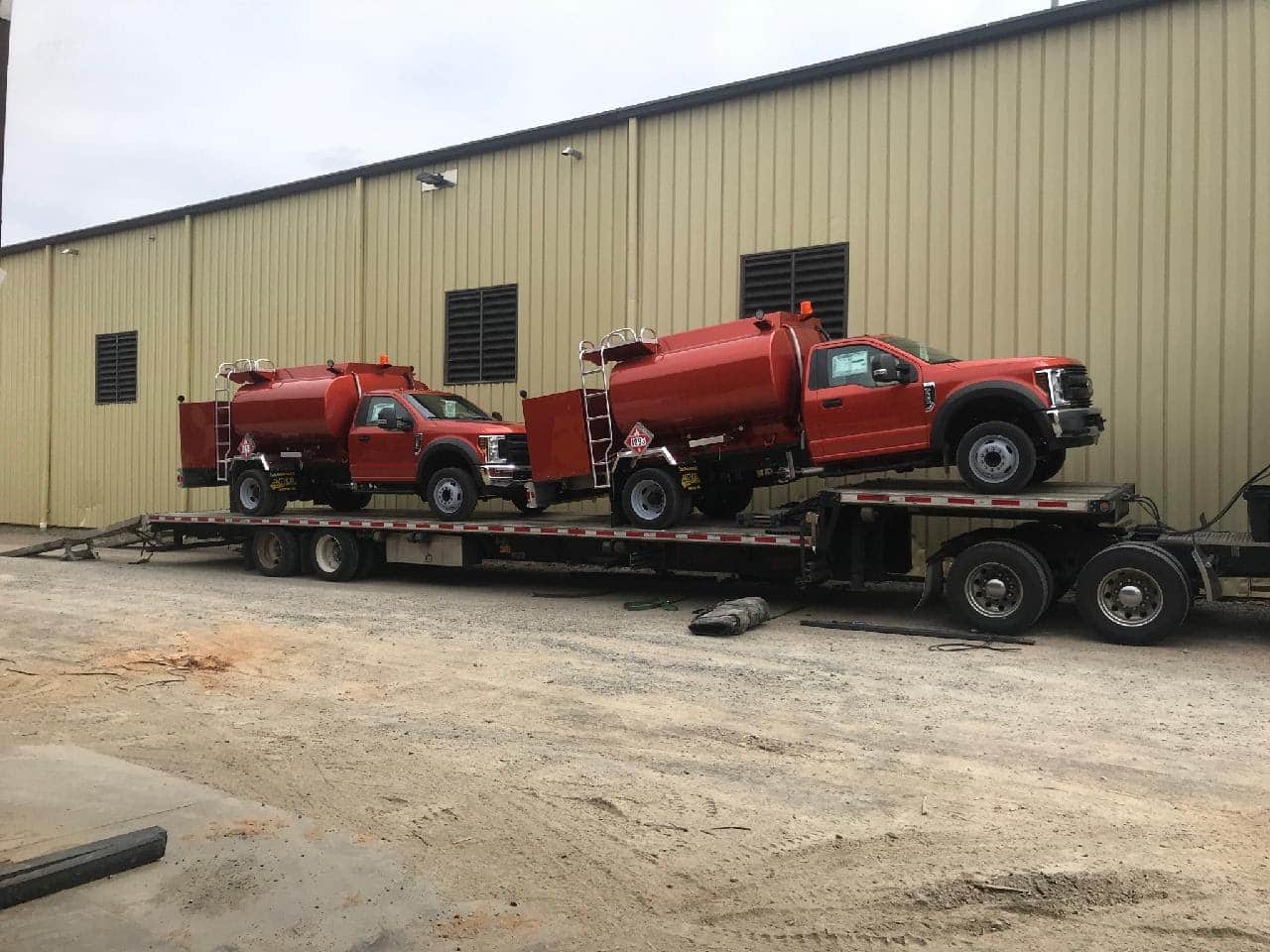 Two Ford F-550 Fuel Trucks loaded on a step deck trailer for transport