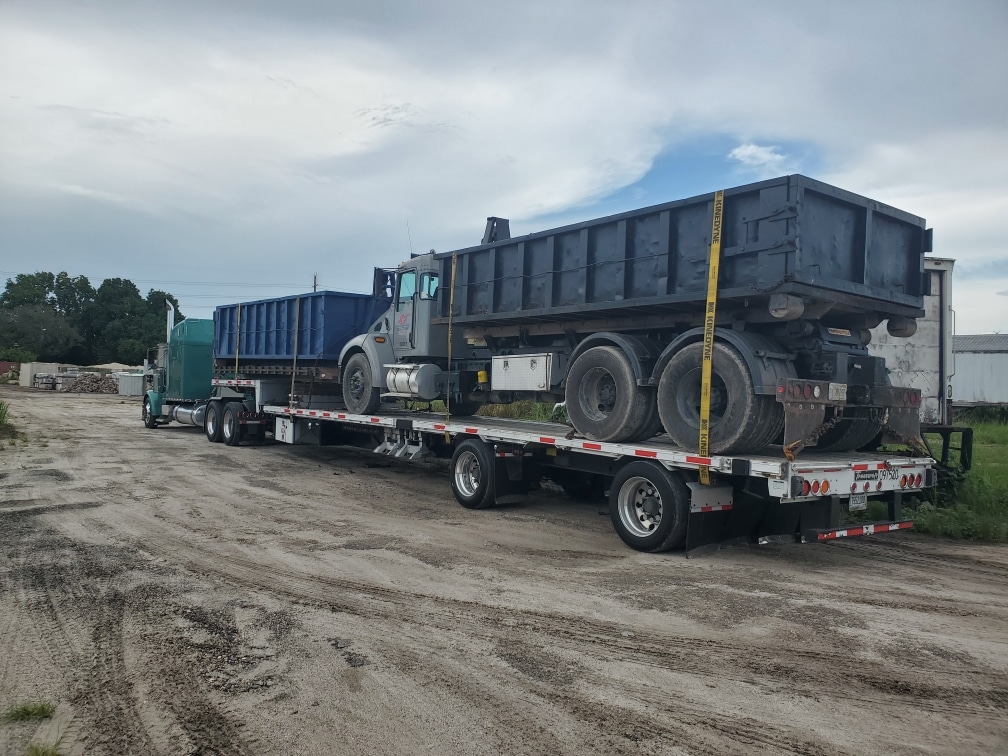 Dump truck loaded with dumpster on a step deck trailer for transport