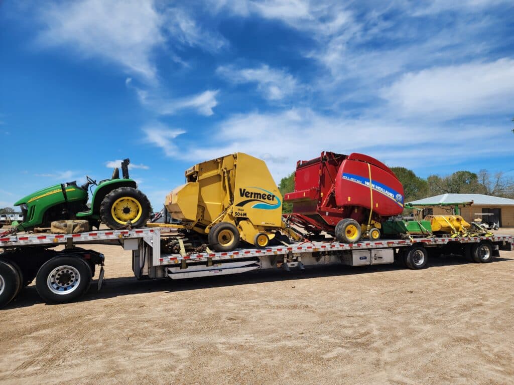 Two balers and a riding mower transported on a step deck trailer.